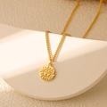 Macro shot of gold sun face pendant necklace resting on a white geometric display - Sun