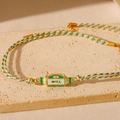 Gros plan d'un bracelet Tarot tressé avec plaque dorée WILL et breloque œil de protection - Oeil du Mal-Vert