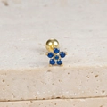 Detail of flower-shaped gold stud earring with blue zircon on beige textured stone - Flower Stud (E1078) / Gold-Dark Blue