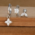 Macro shot of silver earring set with zircon flower charms and leaf stud on wood surface - Silver