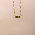 Macro view of a gold pendant featuring a rectangular emerald green zircon stone - August