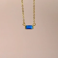 Detailed close-up of a blue rectangular zircon pendant on a delicate gold chain necklace - December