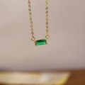 Close-up of a gold chain necklace with a rectangle emerald green stone pendant - May