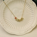 Golden MAMA necklace with red heart birthstone on a ceramic tray for Mother's Day gift - July