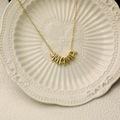 Collier MAMA doré avec pendentif pierre de naissance en poire sur une assiette en porcelaine - Avril