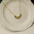 Close-up of gold MAMA necklace with brown birthstone detail on a ceramic dish - August
