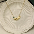 Detail of gold MAMA necklace with blue teardrop gemstone on a white ceramic plate - December