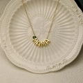 Close-up of gold MAMA necklace with a green teardrop gemstone on a ceramic tray - May