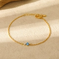 Detail of 18K gold birthstone bracelet with sparkling blue and white round gemstones - October