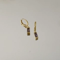 Detailed close-up of gold starburst huggie earrings with purple rectangular gemstones - June