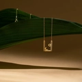 Collar dorado con colgante de sol y luna sobre fondo de hoja tropical verde - Dorado
