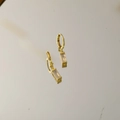 Detail von goldenen Huggie-Ohrringen mit rechteckigem Anhänger auf Spiegeloberfläche - Oktober