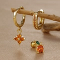 Detailed view of gold clover and orange zircon earrings displayed on a branch - Gold