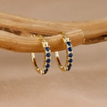 Primer plano de pendientes de aro dorados con piedras azules en una rama de madera - Oro Azul