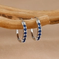 Primer plano detallado de pendientes de aro de plata con circonitas azules en madera - Plateado Azul