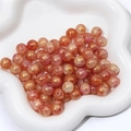 Nahaufnahme von rosa-orangen Glasperlen mit Crackle-Effekt und Goldglitzer auf Weiß - 10mm / Farbe 1