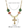 Close-up of golden hollow cross pendant with pearls and green beads on a dainty chain - Cross