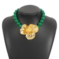 Close-up of a green beaded necklace with a large golden floral pendant on a black bust - Green Gold