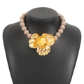 Detailed macro of oversized gold metal floral pendant on light brown beaded necklace - Pink Gold
