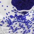 Dunkelblaue transparente Glasperlen 2mm für DIY-Schmuck verteilt in einer weißen Porzellanschale - Saphirblau