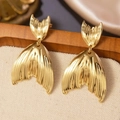 Gros plan de boucles d'oreilles queue de poisson dorées sur un support en bois - Pendentif queue de poisson doré