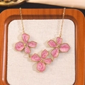 Elegant gold necklace with three pink marble floral pendants on a beige texture mat - Dripping Oil Flower Necklace