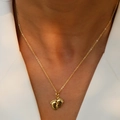 Gros plan d'un collier pendentif pieds de bébé doré porté sur un blazer blanc chic - Style Pieds de Bébé Dorés