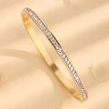 Vergoldetes Edelstahl-Armreif mit eleganten Zirkonia-Steinen auf strukturiertem Hintergrund - Einreihiger Strass-Armreif / Gold
