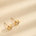 Minimalistische goldene runde Ohrstecker mit klarem Zirkon in Zargenfassung auf beigem Grund - Ohrstecker