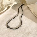 Detail van een minimalistische zwarte hematiet ketting met een kleine kruishanger - Kruis Stijl