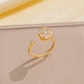 Elegante anillo de titanio dorado con diseño de flor de circón en fondo de seda - Anillo Giratorio Dorado