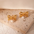 Orecchini a fiocco dorati con perle bianche presentati su pietra beige neutra - Fiocco di Perla Artificiale (BJGE1044)