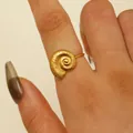 Detailed close-up of a spiral seashell ring in 18K gold plated stainless steel on finger - Conch Style (DZ-1028) / Gold
