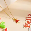 Collier de Noël renne doré avec pendentif cloche en émail rouge sur fond beige chaud - Collier Chapeau à Bois 0787
