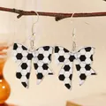 Detailed view of soccer pattern bow earrings hanging on a natural wooden branch - Black & White Soccer Style