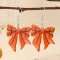 Close-up of basketball pattern bow drop earrings hanging on a natural wooden branch - Orange and Black Basketball Style