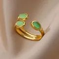 Close-up of 18K gold-plated open ring with three green oval stones on satin fabric - Three Oval Green Cat Eye Stones Style (G10214056)