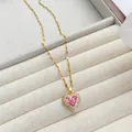 Elegante goldene Titan-Herzenskette mit rosa Zirkonia auf beigem Samttablett präsentiert - Gold - Rot