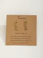 Boucles d'oreilles signe Taureau dorées présentées sur une carte en papier kraft - Taureau-Or