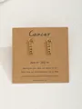 Gros plan de boucles d'oreilles signe Cancer dorées sur carte en papier kraft - Cancer-Or