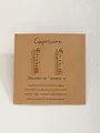Détail de boucles d'oreilles signe Capricorne en métal doré sur support en papier kraft - Capricorne-Or