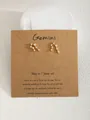 Dettaglio degli orecchini Gemini in oro con zirconi su cartoncino in carta kraft - Gemelli