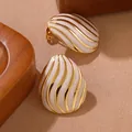Gros plan de boucles d'oreilles dorées avec émail blanc et texture de vagues marines - Style Ovale Larme (FYD6067EH-white)
