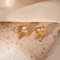 Golden textured feather earrings with white pearls displayed on a beige stone stand - Three Artificial Pearls (BJGE1038)