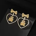 Close-up of golden bow earrings with heart-shaped frame and zircon-encrusted bear charm - Yellow