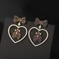 Luxe micro-pave heart and bow earrings with red zircon bear charm on black display - Purple