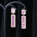 Dettaglio macro di orecchini dorati con zircone rosa rettangolare e pietre bianche - Oro Rosa