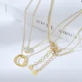 Primo piano di collane placcate oro con anelli intrecciati e pendente in zircone sui libri - Stile Combinato Triplo Anello Diamante Singolo (XL61685) / Oro