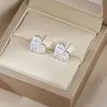 Gros plan de boucles d'oreilles cœur en émeraude verte dans un écrin de luxe - Blanc Argenté