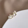 Dettaglio di orecchini a farfalla dorata e fiore di cristallo su supporto bianco raffinato - Oro (Trasparente)